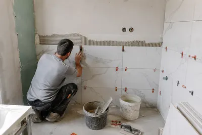 Tegelzetter plaatst grote wandtegels in een nieuwe badkamer